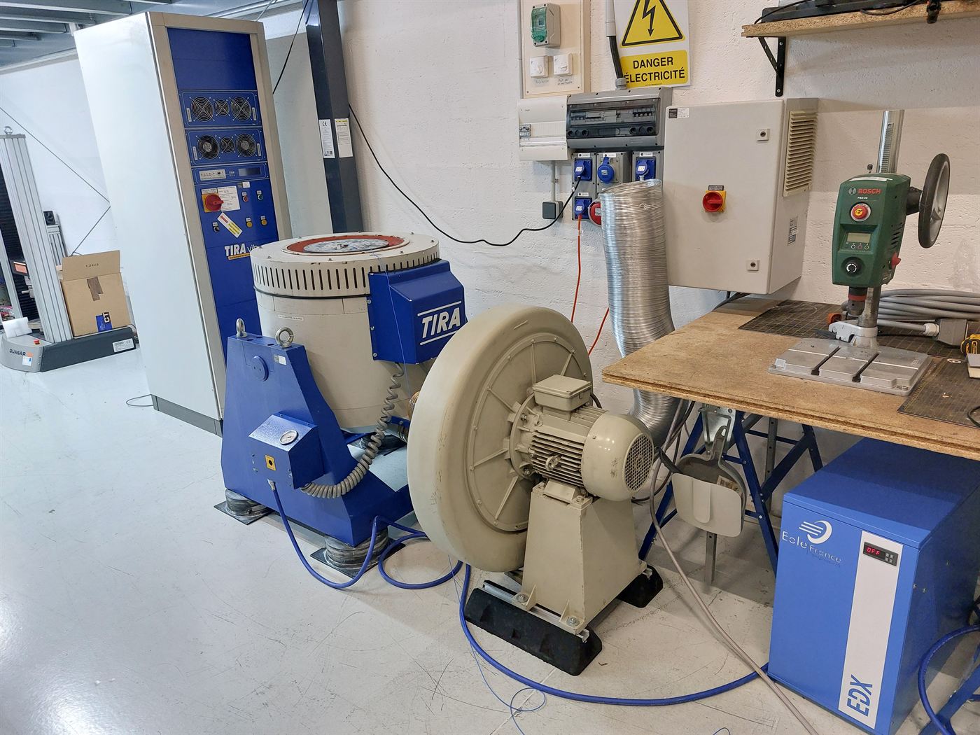 An electrodynamic shaker and its amplifier cabinet on the workshop floor, used for vibration testing of flight hardware.